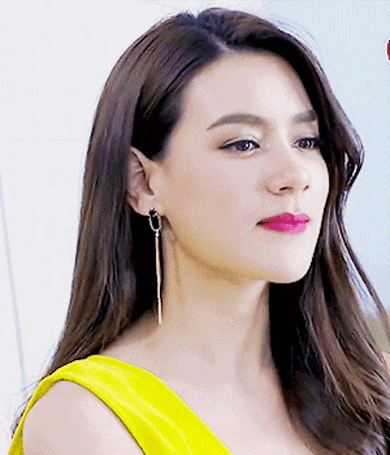a close up of a woman 's face wearing earrings and a yellow top