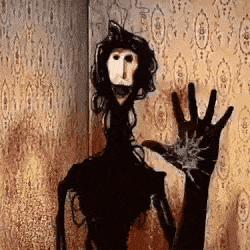 a creepy doll is waving at the camera in front of a wall with a patterned wallpaper .