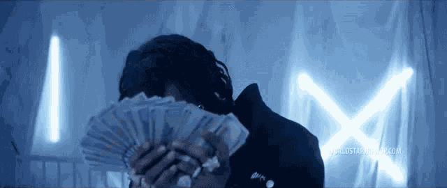 a man is holding a fan of money in front of his face in a dark room .