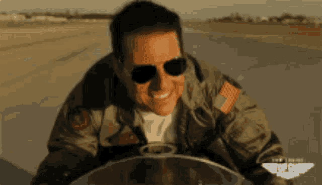 a man wearing sunglasses and a top gun jacket smiles
