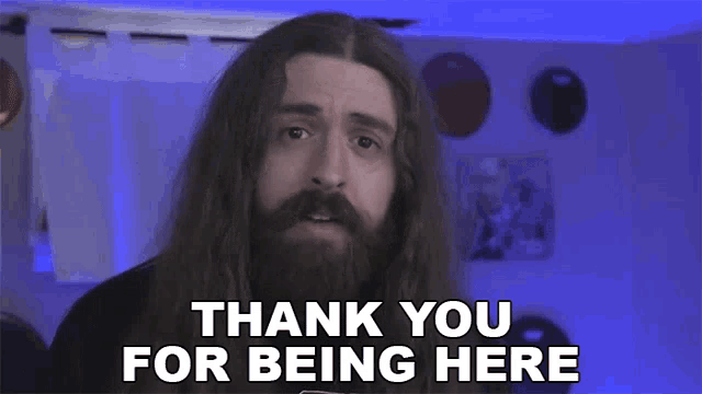 a man with long hair and a beard is giving a thank you for being here speech .