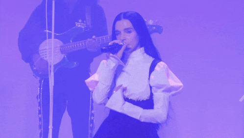 a woman sings into a microphone while a man plays a guitar in the background