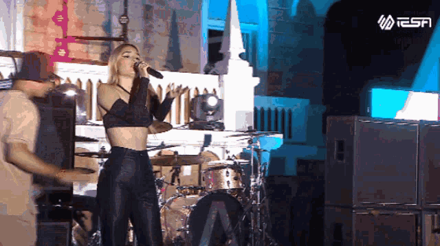 a woman sings into a microphone while a man plays drums in front of a tesa logo