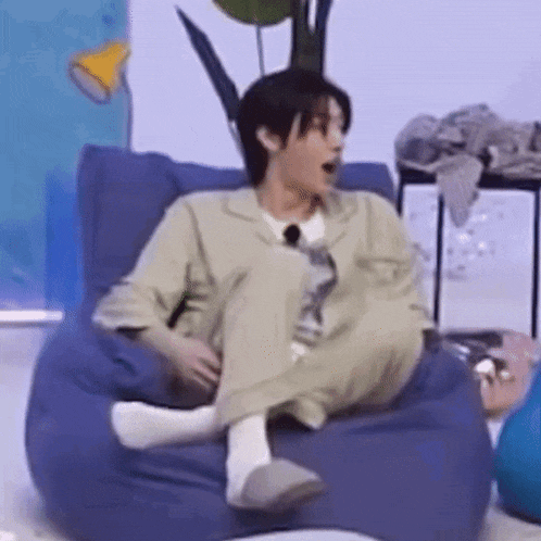 a man is sitting on a bean bag chair with his legs crossed and yawning .