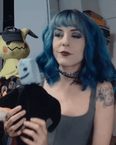 a woman with blue hair and a tattoo on her arm is holding a stuffed animal