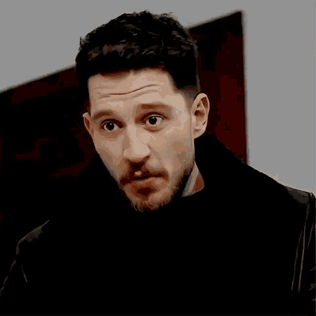 a man with a beard and a black jacket is giving a thumbs up sign .
