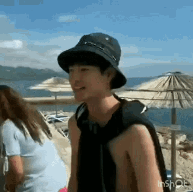 a man wearing a hat is standing on a beach next to a woman .