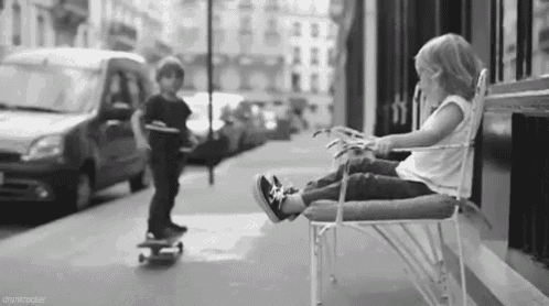 a boy is riding a skateboard while a girl sits on a chair .
