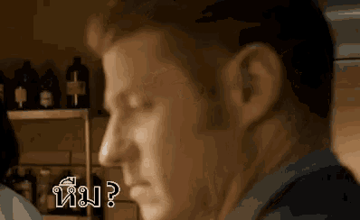 a man is standing in front of a shelf with bottles on it and asking a question in a kitchen .