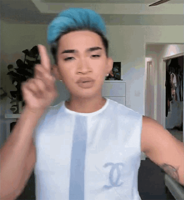 a man with blue hair is wearing a white tank top with a chanel logo on the front