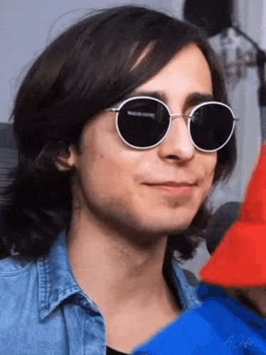 a man wearing sunglasses and a blue shirt is smiling .