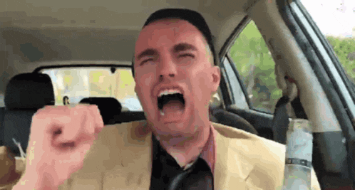 a man in a suit and tie is screaming in a car