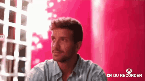 a man in a striped shirt is sitting in front of a pink wall with the words du recorder on the bottom right