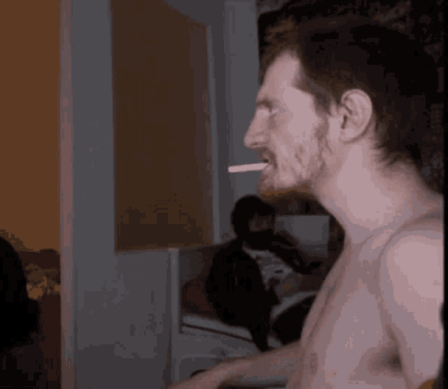 a shirtless man is smoking a cigarette in a dark room