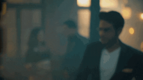 a man in a suit and white shirt is standing in a dark room .