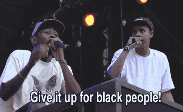 a man singing into a microphone with the words give it up for black people behind him .