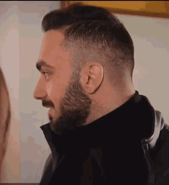 a man with a beard is wearing a black leather jacket and a black turtleneck .