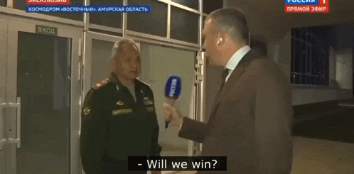 a man in a suit is talking to a man in a military uniform while holding a microphone .