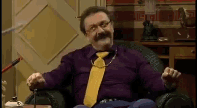a man in a purple shirt and a yellow tie is sitting in a chair