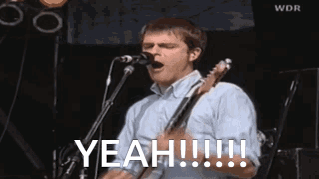a man singing into a microphone while holding a guitar with the word yeah written on the bottom