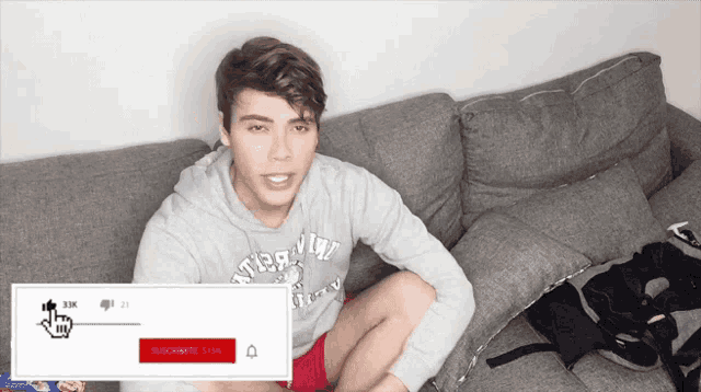 a young man is sitting on a couch wearing a grey sweater that says abercrombie & fitch