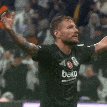 a man wearing a black beko jersey holds his arms up in the air