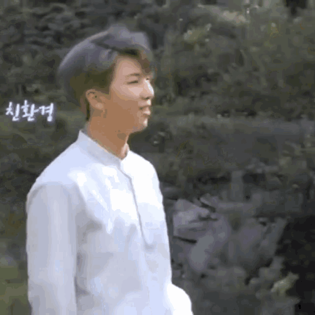 a young man wearing a white shirt is standing in front of a river .