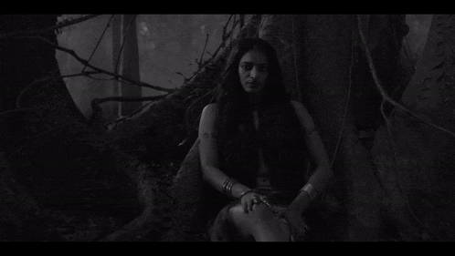 a black and white photo of a woman sitting under a tree in the woods .