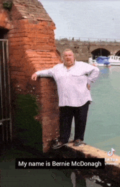 a man leaning against a brick wall next to a body of water with the caption " my name is bernie mcdonald "