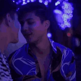 a couple of men are kissing in front of a blue light .