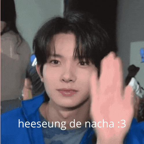 a young man in a blue jacket is waving his hand with the words heeseung de nacha : 3 below him