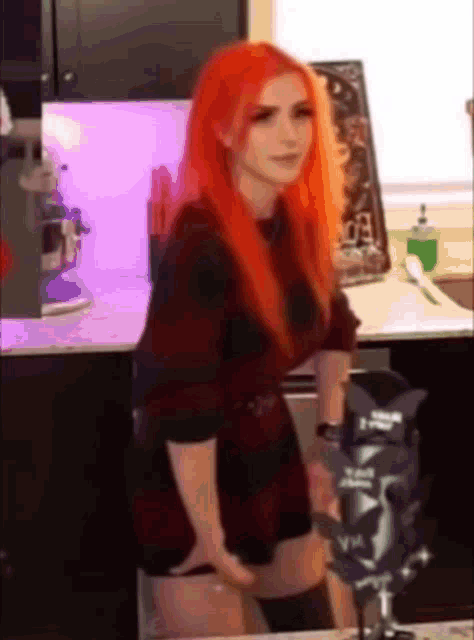 a woman with red hair is standing in front of a microphone in a kitchen
