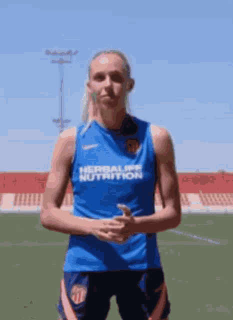 a woman is standing on a soccer field wearing a blue shirt that says herbalife nutrition on it .