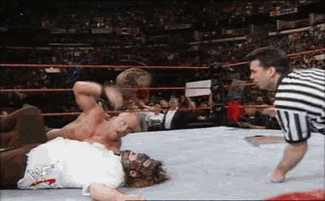 two men are wrestling in a wrestling ring and a referee is standing between them .