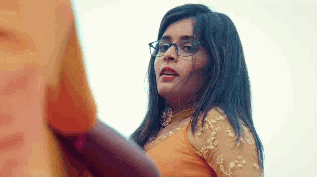 a close up of a woman wearing glasses and an orange dress .