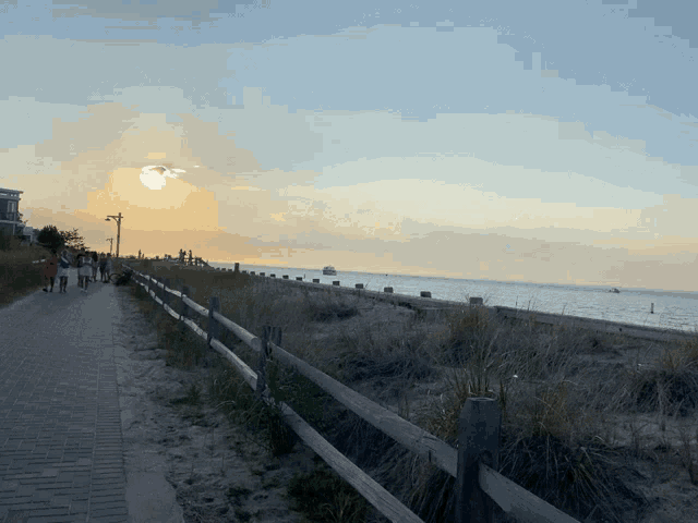 a group of people walking along a path near the ocean at sunset