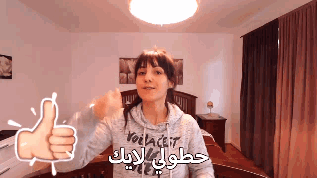 a woman giving a thumbs up in front of a bed wearing a sweatshirt that says voilacert