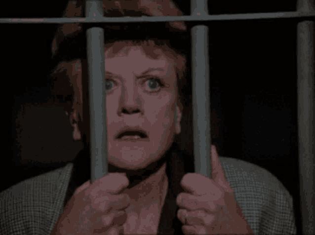a woman is behind bars in a jail cell with a serious look on her face