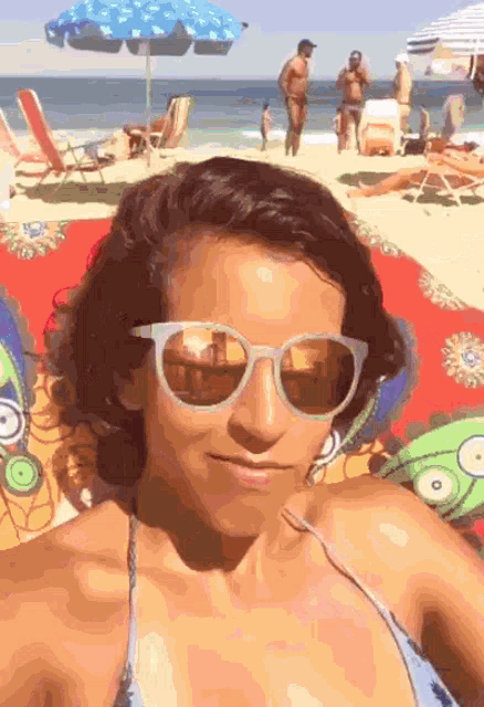 a woman wearing sunglasses takes a selfie at the beach