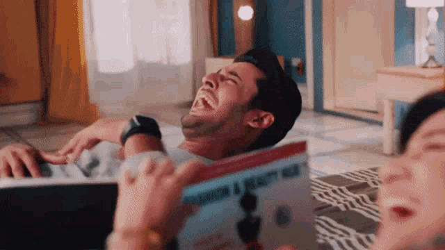 a man is laying on the floor laughing while a woman holds a book titled fashion & beauty