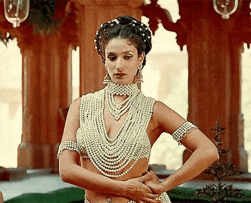 a woman wearing a pearl necklace and bracelets is standing with her hands on her hips .