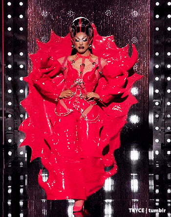 a drag queen in a red dress is walking on a stage .