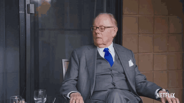 an older man in a suit and tie is sitting in front of a netflix logo