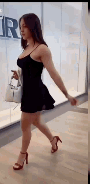 a woman in a black dress and heels is walking down a hallway .