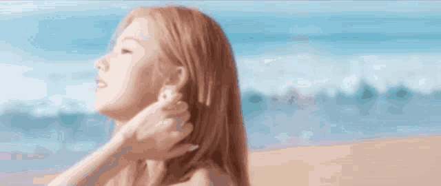 a woman is standing on a beach with her eyes closed and touching her neck .