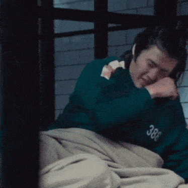 a man in a green shirt is laying in bed with a blanket on .