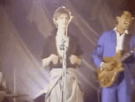 a man in a blue suit is playing a guitar next to a woman singing into a microphone .