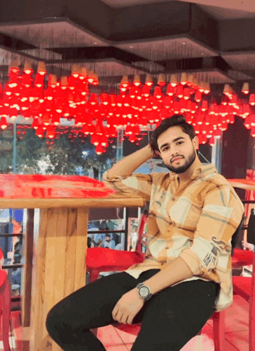 a man in a plaid shirt sits in front of a table with red lights hanging from the ceiling