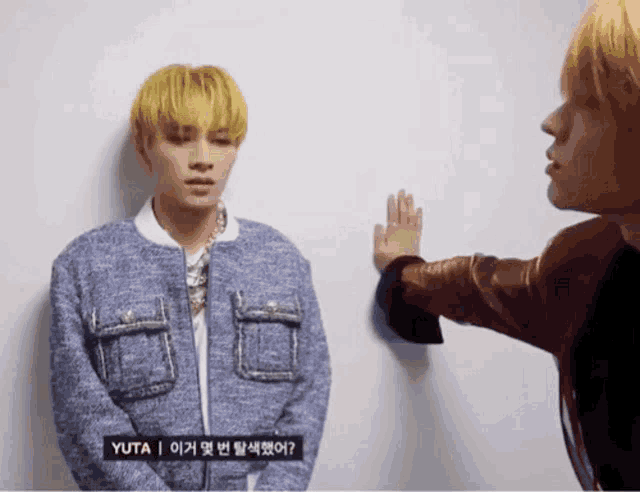 a man in a blue jacket is standing next to another man with yellow hair
