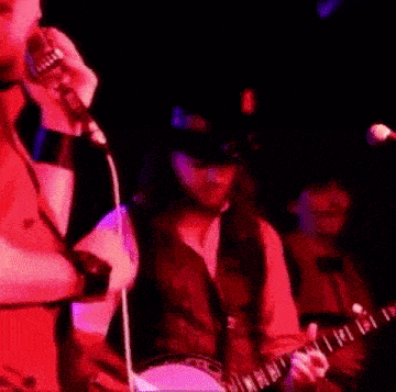 a man is singing into a microphone while a man plays a banjo on stage .